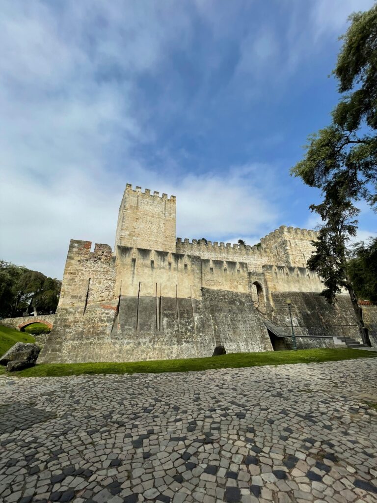 Low angle view of the historic Sao Jorge Castle against a blue sky with clouds.