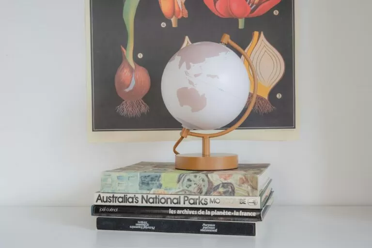 A stylish globe resting on a stack of books with botanical art in the background, representing education and exploration.