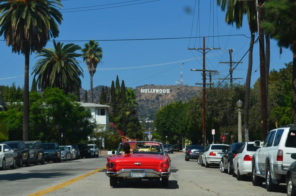 Red convertible driving down a sunny street towards the iconic Hollywood sign in Los Angeles.