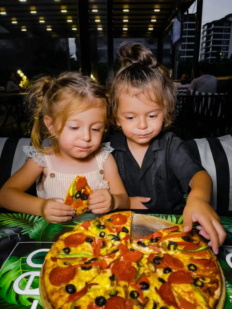 Two young girls delightfully eating pizza at an outdoor restaurant setting. Perfect family meal moment.