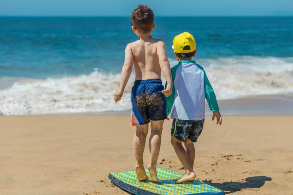 Two children playing on the beach with a bodyboard, enjoying a sunny day by the ocean.