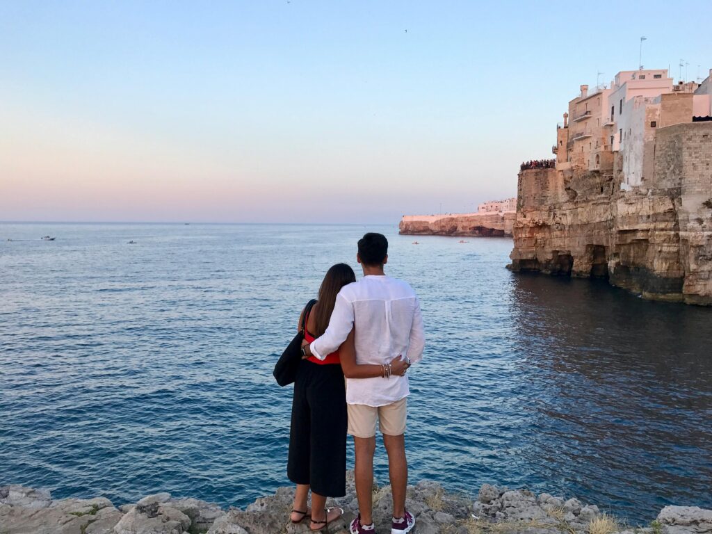 Couple embraces by the sea in Polignano A Mare, Italy, during sunset.