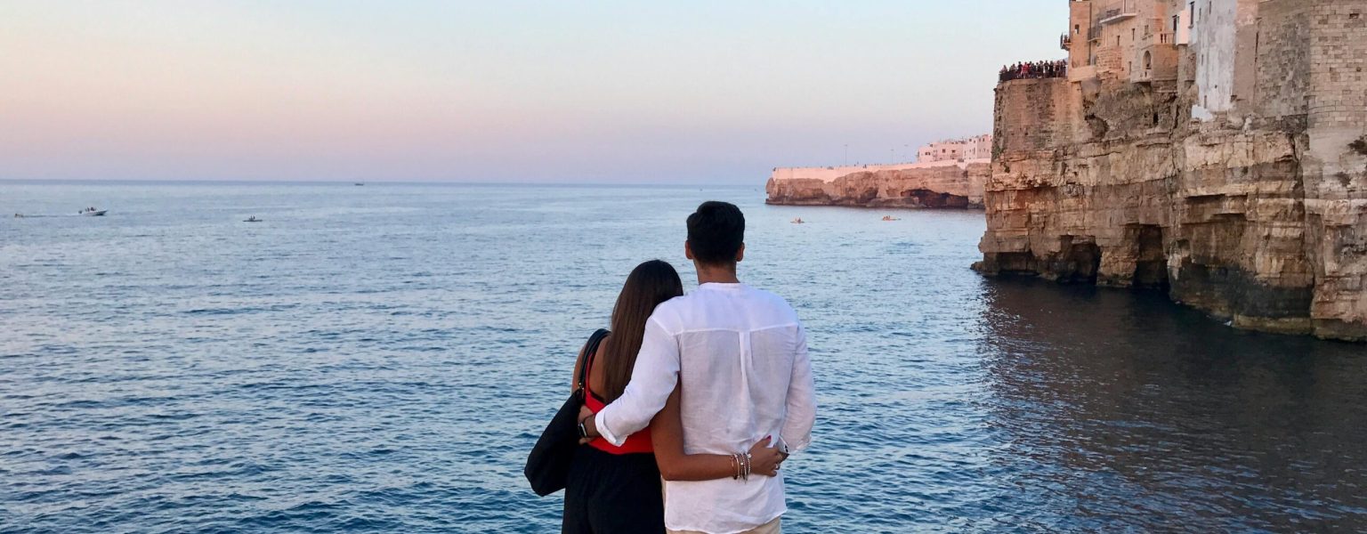 Couple embraces by the sea in Polignano A Mare, Italy, during sunset.