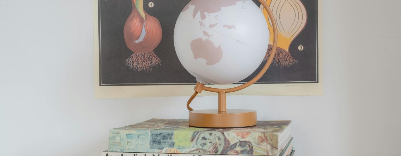 A stylish globe resting on a stack of books with botanical art in the background, representing education and exploration.