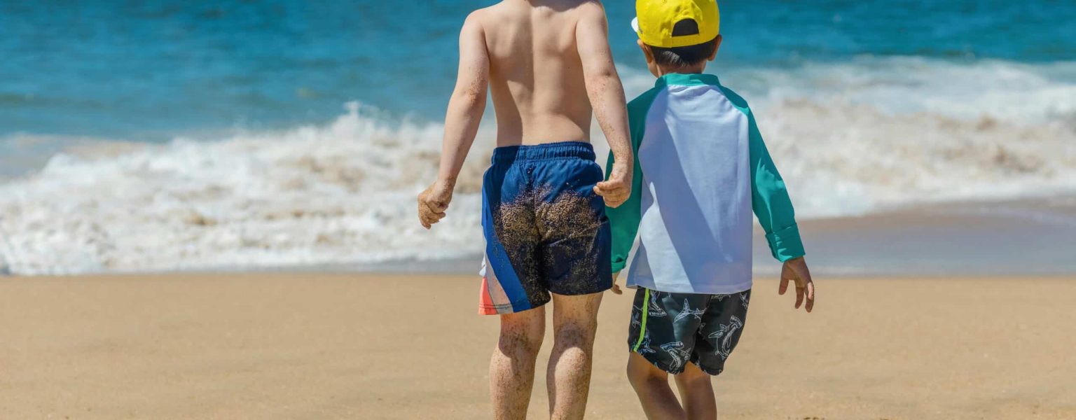 Two children playing on the beach with a bodyboard, enjoying a sunny day by the ocean.